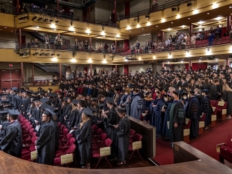 Students standing in rows of seats in cap & gowns in Duke Family Performance Hall 