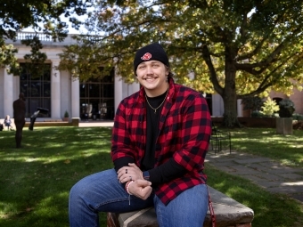 Jake Fernicola, a male student in a black beanie hat and red flannel sitting outside