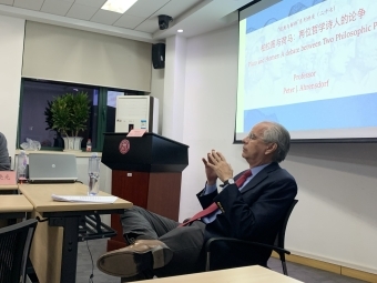 Professor lecturing at a table with powerpoint behind him