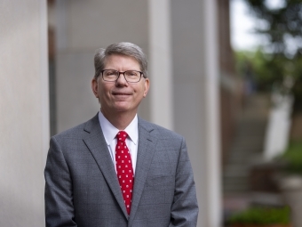 A white male wearing a grey suit and a red tie