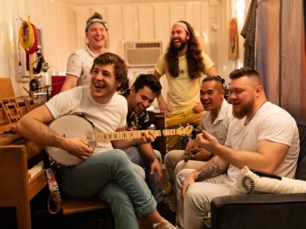 A group of young men sitting together and smiling while one holds a banjo