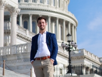 a young man wearing a jacket and collared shirt stands on the steps of the U.S. Capitol