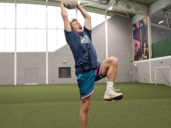 a male wearing athletics throws a soccer ball while in an indoor field