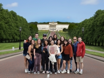 a group of students stand in front of a large white structure with a sprawling green lawn in front