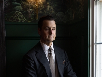 a young white man wearing a suit sitting in a dark room with a lamp behind