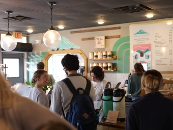 a group of students smile and talk while waiting in line at a coffee shop