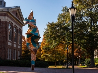 a brick building surrounded by trees with fall foliage and a colorful sculpture