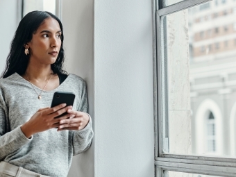 Woman holding a cell phone looking out the window wondering about social media misinformation