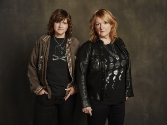 two women standing by each other over a dark background