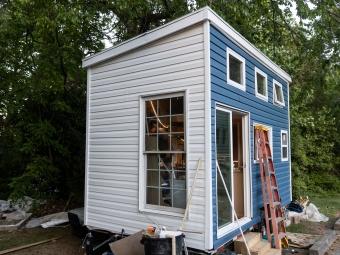Exterior of tiny house during painting process, half white and blue