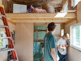 Students inside the tiny house, using a drill on the window sill