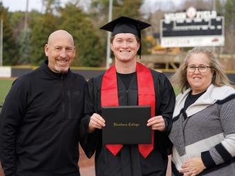 Nolan DeVos ’23 holding his diploma standing between parents