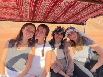 a group of four young women smiling together in a desert environment