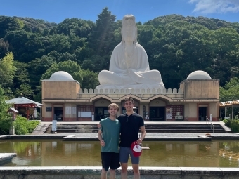 two young men stand in front of a temple