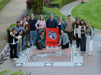 a group of students and some older people at an old castle holding a "Davidson College" banner