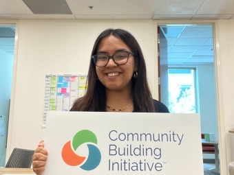 a young woman holds a sign that says "community building initiative"