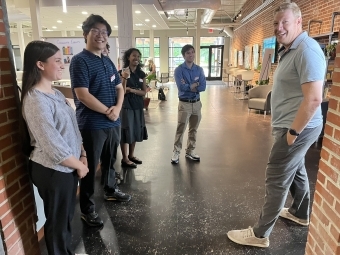 a group of students and professors stand around a modern office space talking and smiling