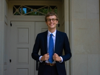 a young white man wearing a suit and tie standing in front of an old building