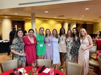 a group of young women in dresses and nametags smile standing together