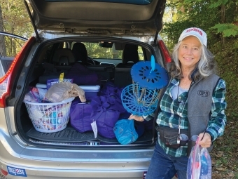 a woman poses in front of a car trunk filled with supplies for hurricane relief