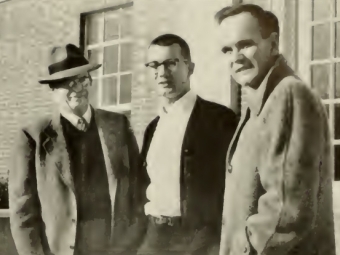 Soccer coaches McCutchan and Marrotte with captain Ross Smyth standing in front of a building on campus