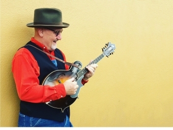 Mike Compton playing the mandolin against a yellow wall