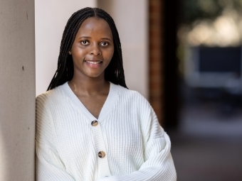 a young Black woman wearing a white sweater leaning against a column