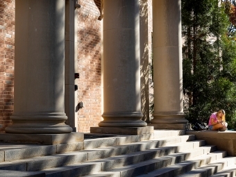 a student sits on the steps of an academic building reading a book