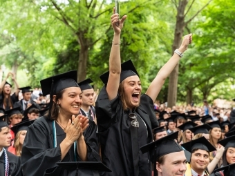 two young women in graduation regalia cheer with their hands in the air