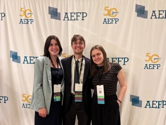 a group of three students in business casual smile together at a conference