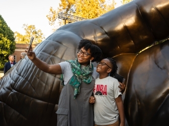 two young people smile and take a selfie in front of a sculpture