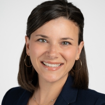 a woman with brown hair wearing a white top and blazer