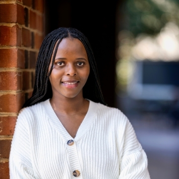 a young Black woman leaning against a brick wall wearing a white sweater