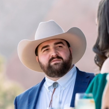 a young white man wearing a cowboy hat with facial hair smiling