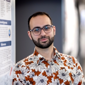 a young man wearing a Hawaiian shirt and glasses standing in front of a scientific research poster