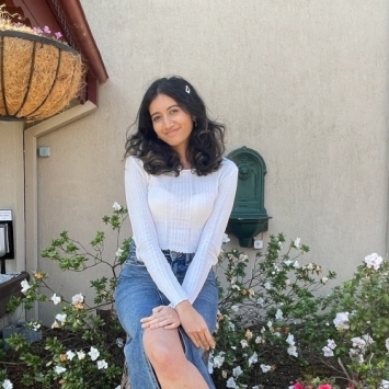 a young woman wearing a white top and denim skirt sitting in an outdoor garden