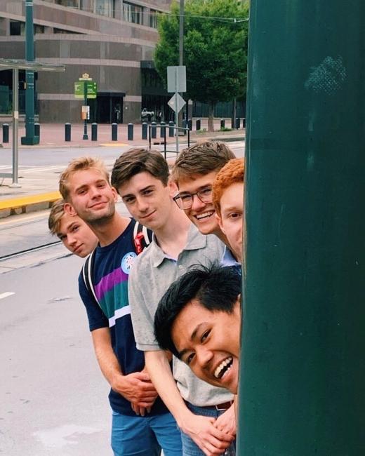 Group of boys stick their heads out from behind a pole