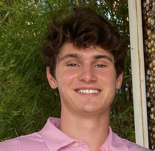 a young white man with brown hair smiling and wearing a pink shirt