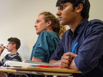 Three students sit at desk looking ahead during a political science class