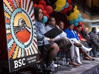 panel of people on stage with a sign in foreground that says "BSC Celebrating 50+ Years"