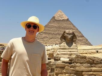 a young white male wears a straw hat while standing in front of an Egyptian pyramid and sphinx